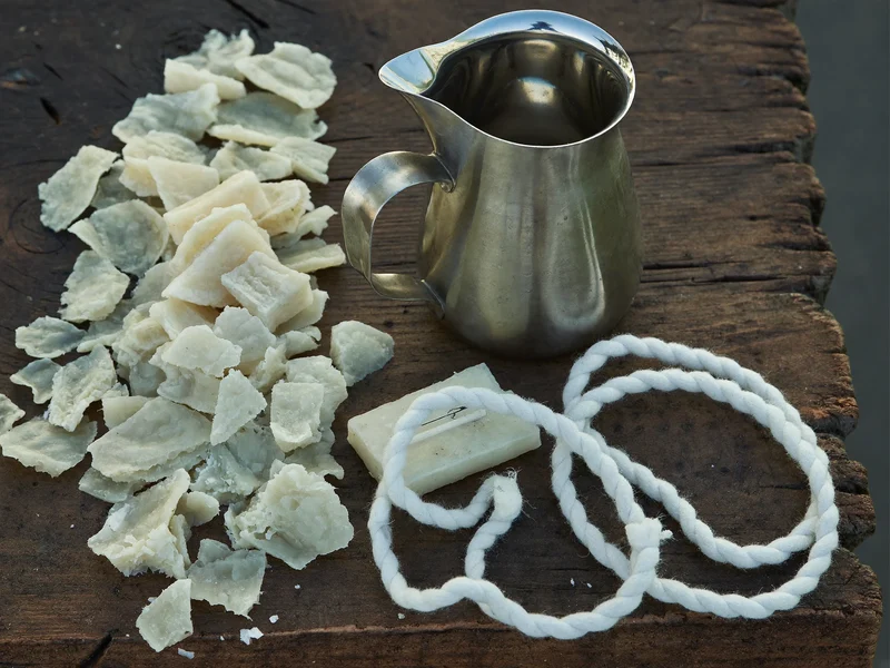 Scaglie di cera di soia, stoppini in cotone e brocca da colata sul banco